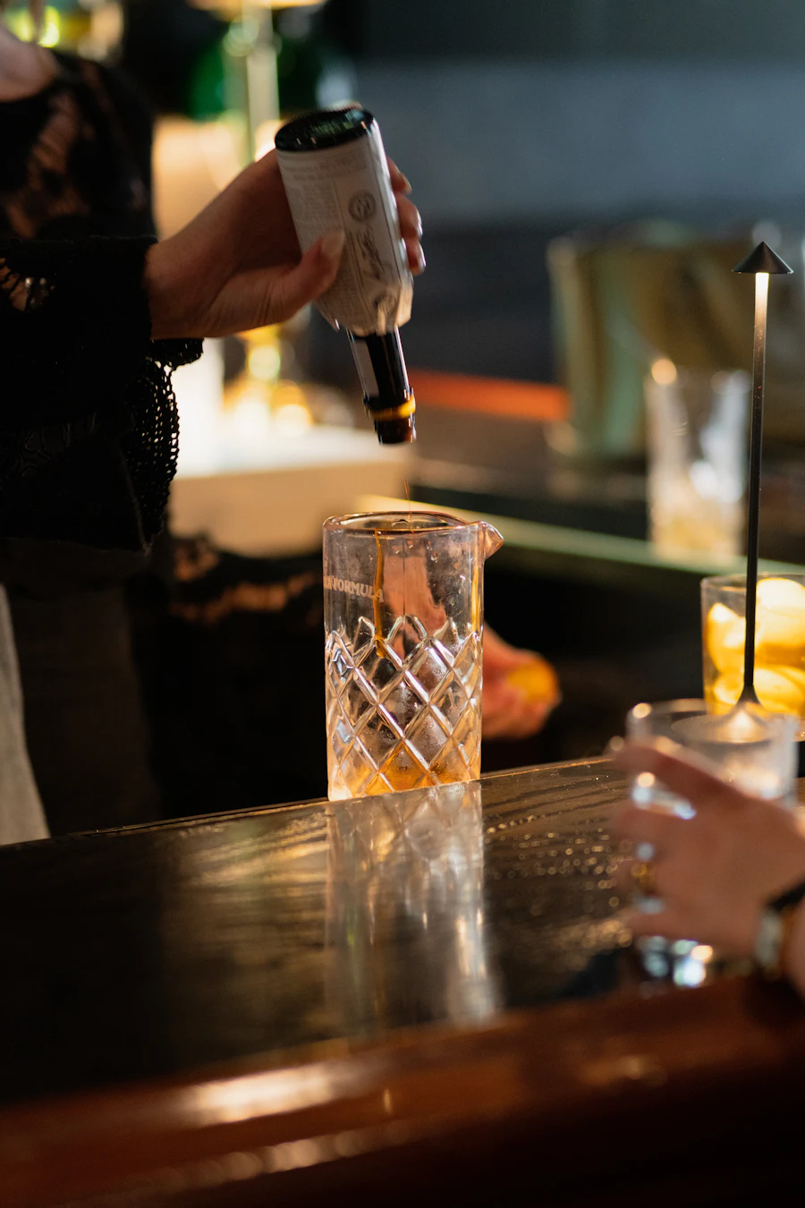 A bartender pours a cocktail at a dark bar, late in the night