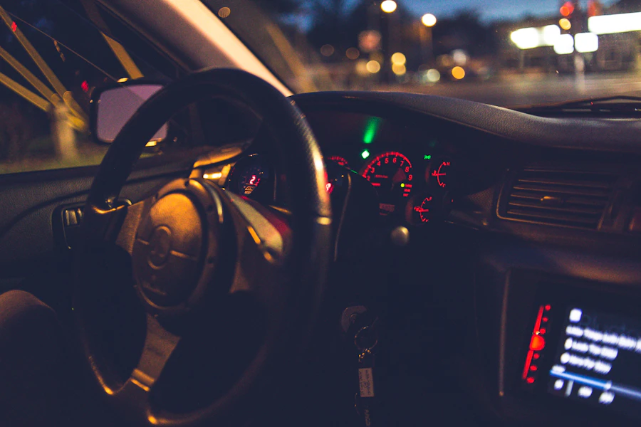 Steering wheel and dashboard of a car at night, city lights visible through the windshield